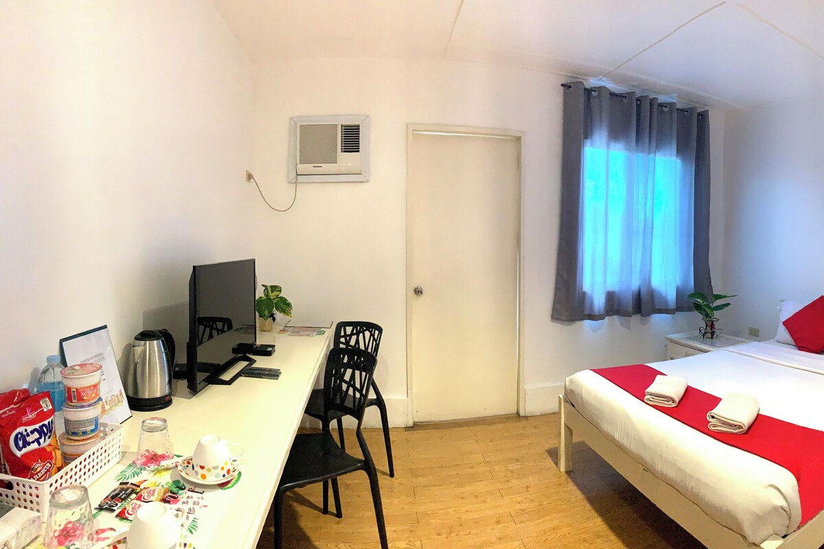 Une chambre d’hôtel comprenant un lit, un bureau avec un ordinateur, une chaise, une fenêtre avec des rideaux, un tableau au mur, ainsi qu’une salle de bain avec une douche et des toilettes.