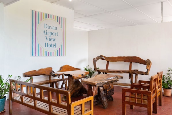 Une pièce meublée de façon rustique, avec des meubles en bois, notamment un banc et des chaises, et une pancarte sur le mur indiquant : « Hôtel Davao Airport View ».