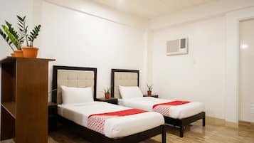 A hotel room with two beds, a wooden wardrobe, and a potted plant.