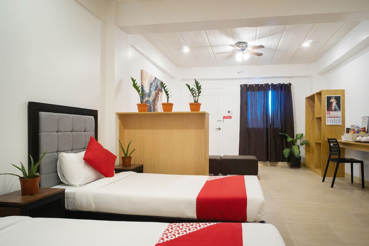 Une chambre d’hôtel avec deux lits, un bureau, une armoire et un ventilateur de plafond.