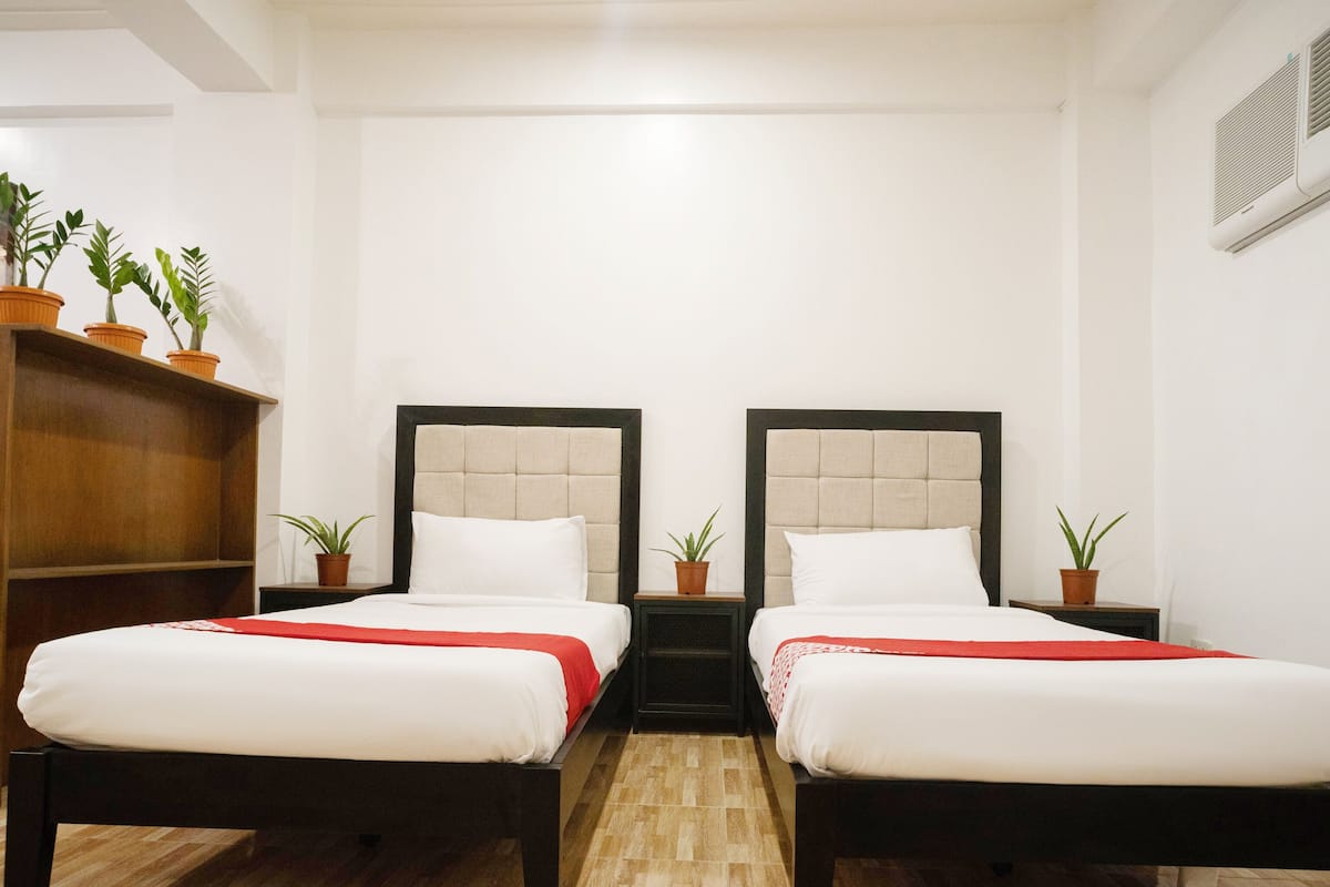 Une chambre double avec deux lits, chacun doté d’une tête de lit, d’une armoire en bois et de plantes en pot.