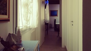 A narrow hallway with a wooden ceiling, a bed with a blue bedspread, a white bottle, and a framed picture on the wall. - Le mille e una notte (Comacchio)