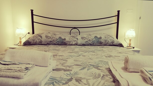 A neatly made bed with floral bedding, two bedside lamps, and folded towels on the bed. - Le mille e una notte (Comacchio)