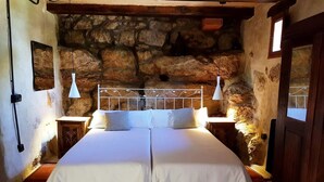 A double bed with white linens in a rustic room with stone walls and wooden beams. - Masia Heredad La Boquilla (Enguera)
