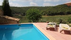 A swimming pool with lounge chairs and a table with fruits and a glass of orange juice. - Masia Heredad La Boquilla (Enguera)