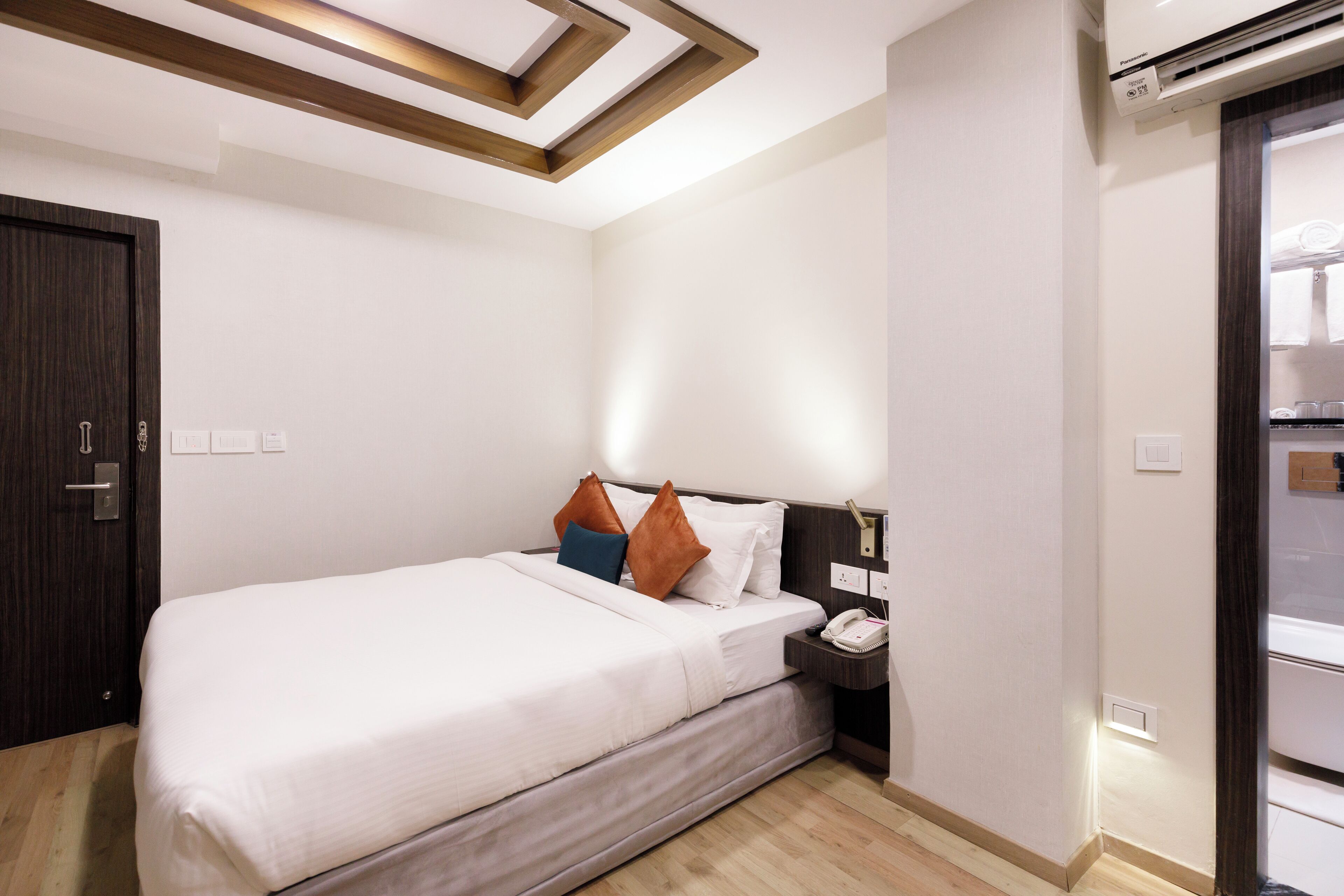 A hotel room with a bed, bedside table, and an air conditioning unit.