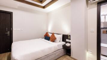 A hotel room with a bed, bedside table, and an air conditioning unit.