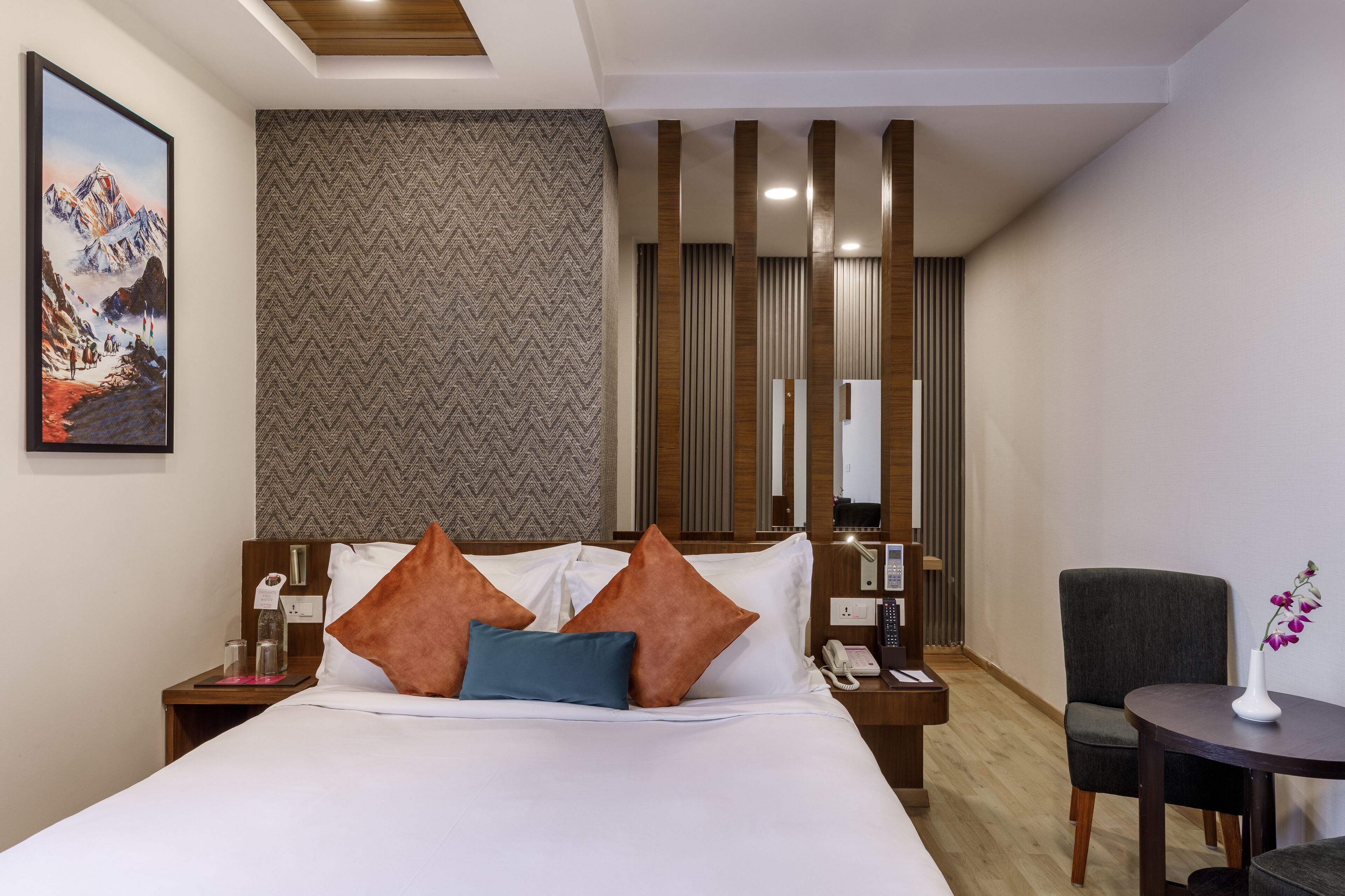 Habitación de hotel con cama, mesita de noche, una silla, una pequeña mesa y un cuadro en la pared.