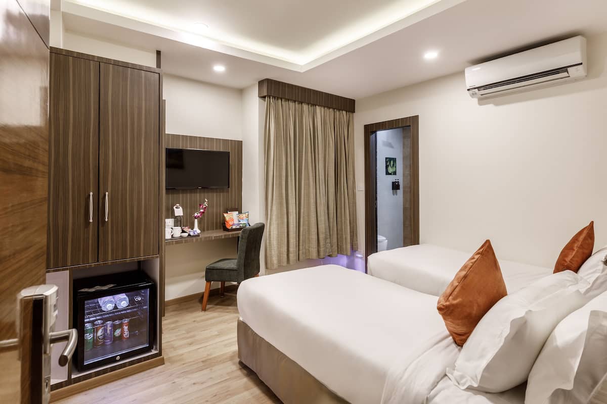 A hotel room with a bed, a desk with a computer, a TV, and an air conditioner.