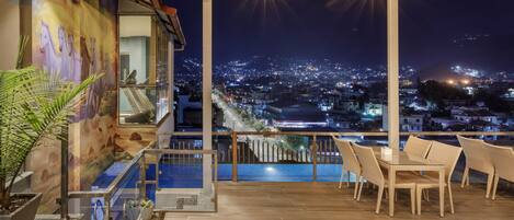 Une terrasse sur le toit avec une piscine, un espace salon et une vue sur la ville la nuit.