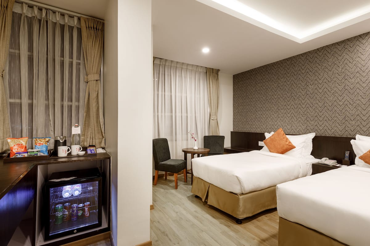 A hotel room with two beds, a desk with a refrigerator, a chair, a small table, and curtains.