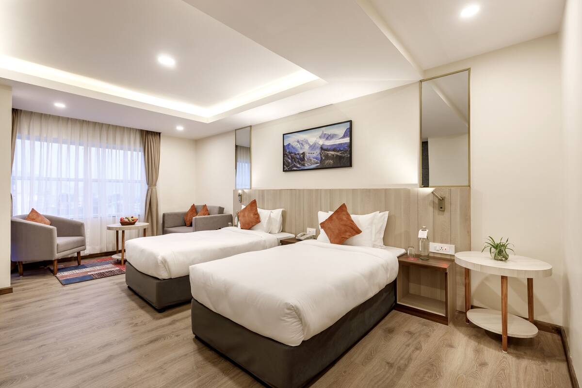 A hotel room with two beds, a sitting area with a sofa and armchairs, a small table, a round side table, and a large mirror.