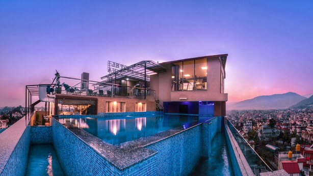 A modern hotel with a rooftop infinity pool, a terrace with seating, and a city view.