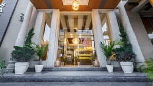A hotel entrance with a modern design, featuring large columns, a glass facade, and potted plants.