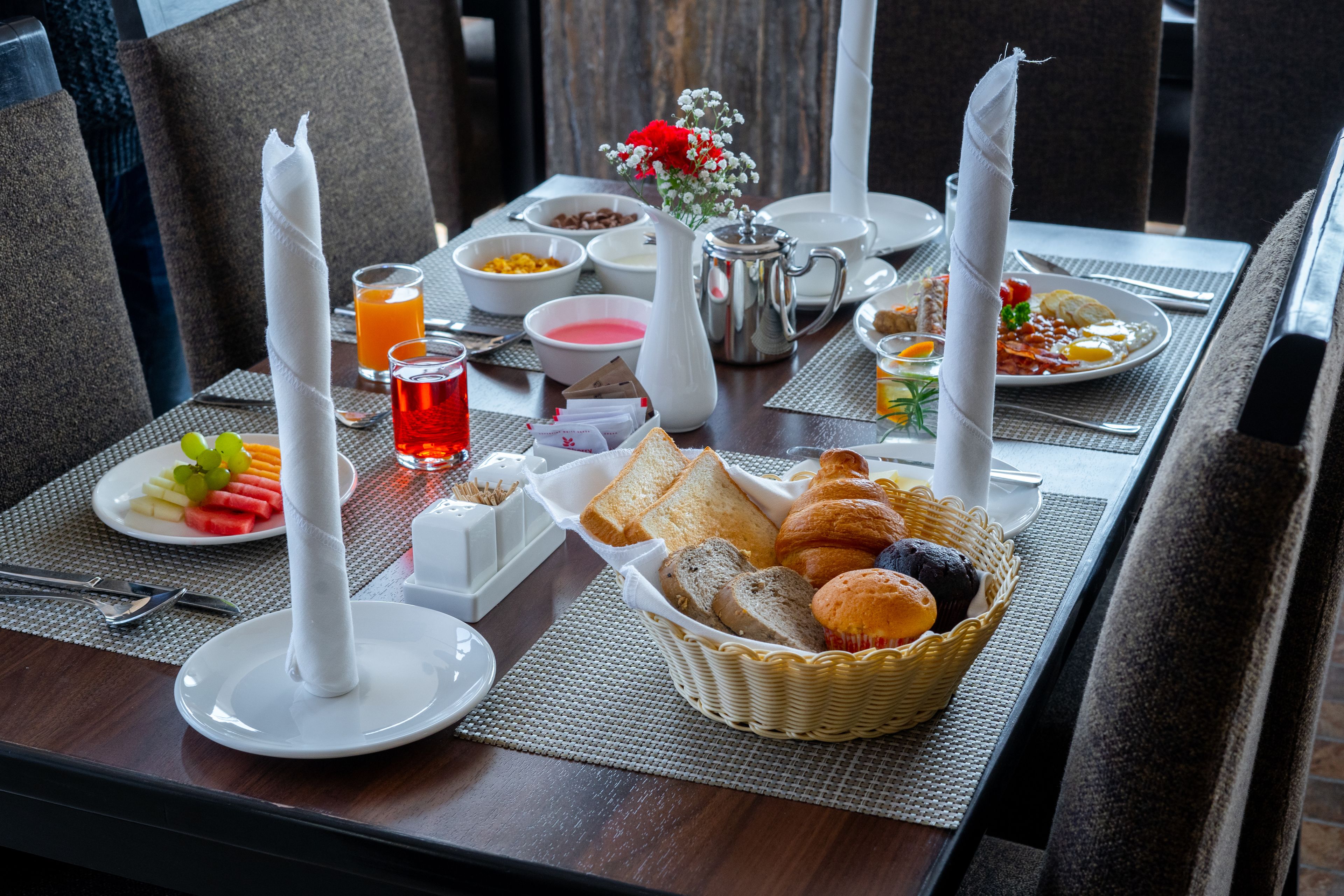 A breakfast table set with plates, bowls, a basket of bread, and a vase of flowers.