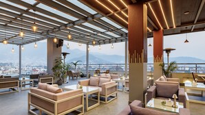 A modern lounge area with comfortable seating, large windows, and a view of the city and mountains.