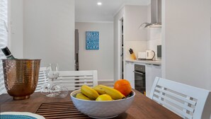 A dining area with a wooden table, a bowl of fruit, and a copper cocktail bowl. - Beautiful , stylish Mudjimba Beach House (Mudjimba)