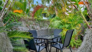 An outdoor dining area with a glass table and black chairs, surrounded by lush tropical plants and a bamboo fence. - Beautiful , stylish Mudjimba Beach House (Mudjimba)