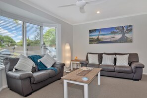 A living room with two leather sofas, a coffee table, a floor lamp, and a beach scene painting on the wall. - Beautiful , stylish Mudjimba Beach House (Mudjimba)