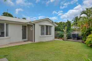 A single-story house with a well-maintained lawn, a patio with outdoor furniture, and a variety of tropical plants. - Beautiful , stylish Mudjimba Beach House (Mudjimba)