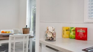 A kitchen with white cabinets, a granite countertop, and a window with blinds. There is a bowl of fruit, a glass, and a jar of seashells on the counter. - Beautiful , stylish Mudjimba Beach House (Mudjimba)
