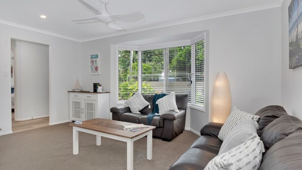 A modern living room with a sofa, a coffee table, and a ceiling fan. - Beautiful , stylish Mudjimba Beach House (Mudjimba)