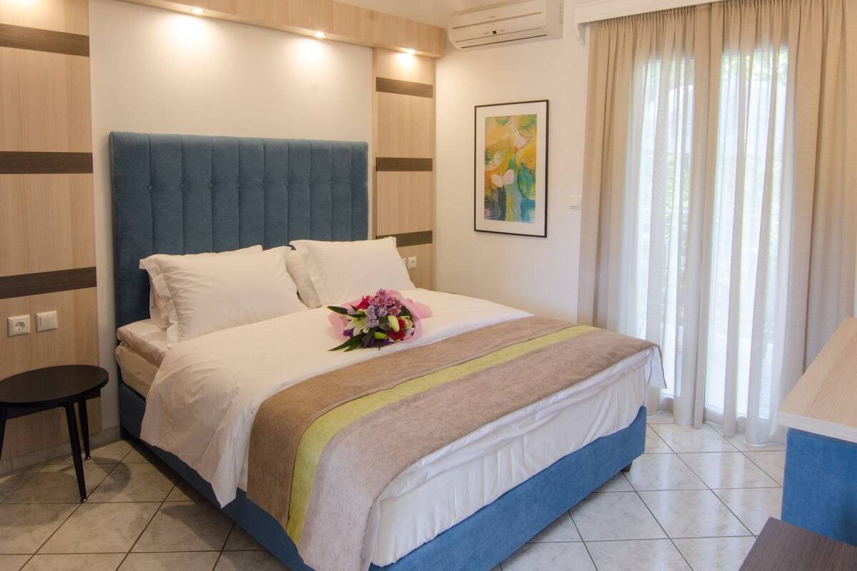 Habitación de hotel con una cama grande, una mesita de noche, aire acondicionado instalado en la pared y una ventana con cortinas.