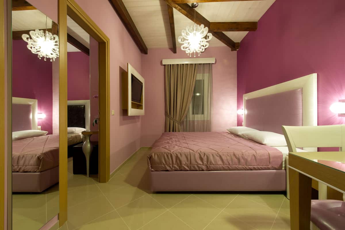 Un dormitorio con pared rosa, una cama con cabecera, una mesita de noche, un espejo y una araña.