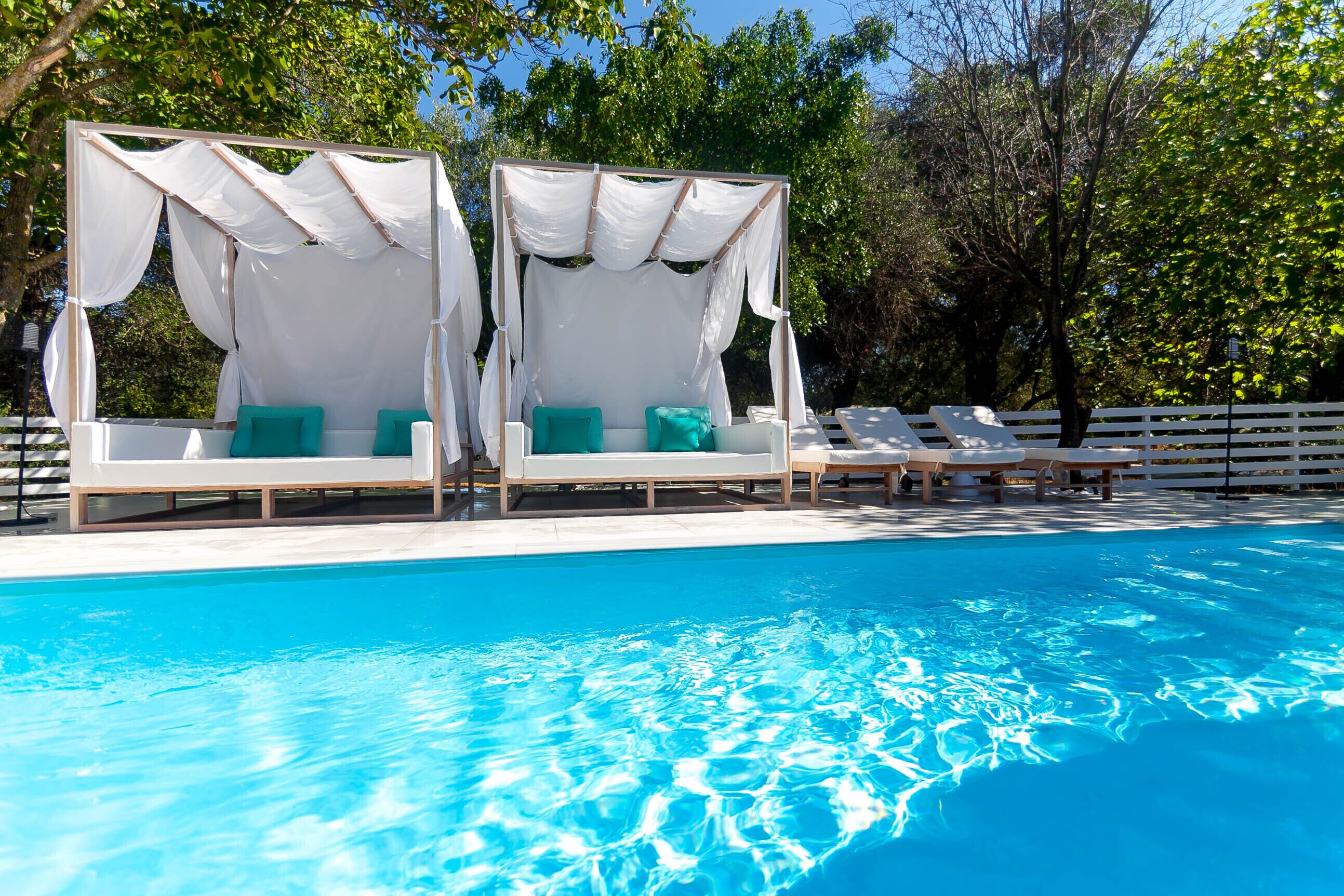 A pool area with two white canopy beds and lounge chairs.