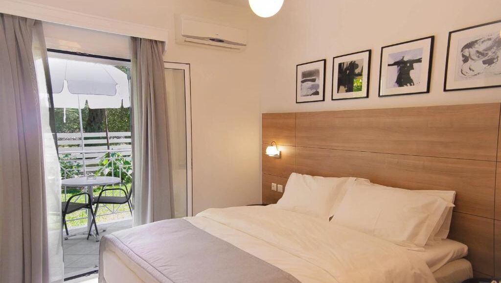 Quarto de hotel com cama, mesa de cabeceira, luminária na parede e janela com cortinas.