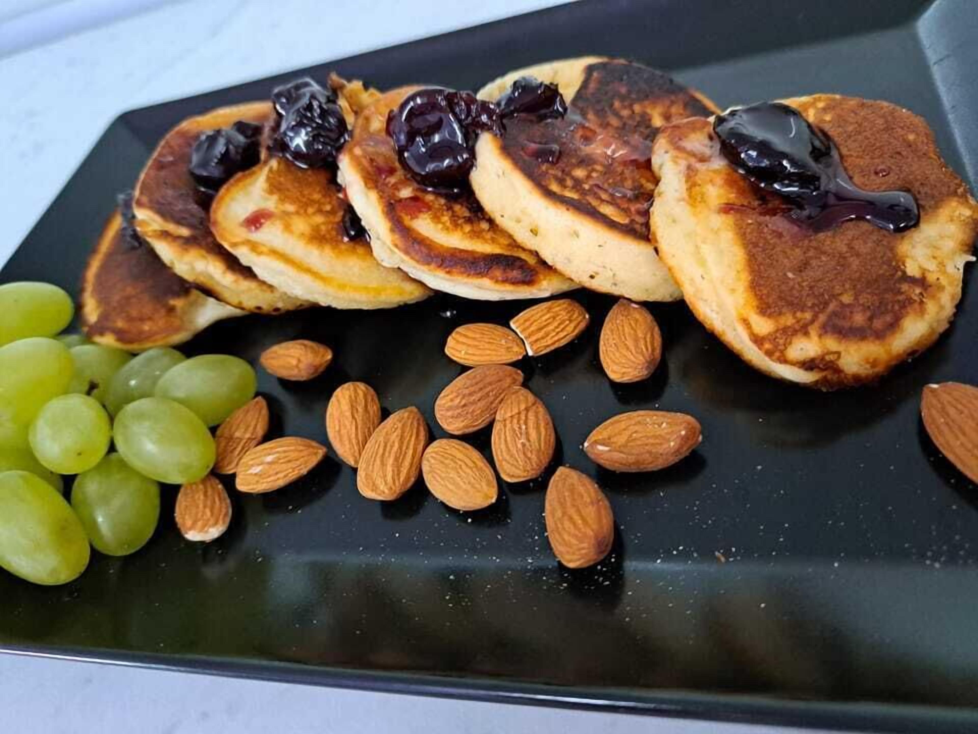 A plate with pancakes topped with dark syrup, accompanied by almonds and green grapes.