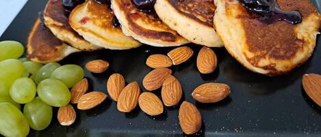 A plate with pancakes topped with dark syrup, accompanied by almonds and green grapes.