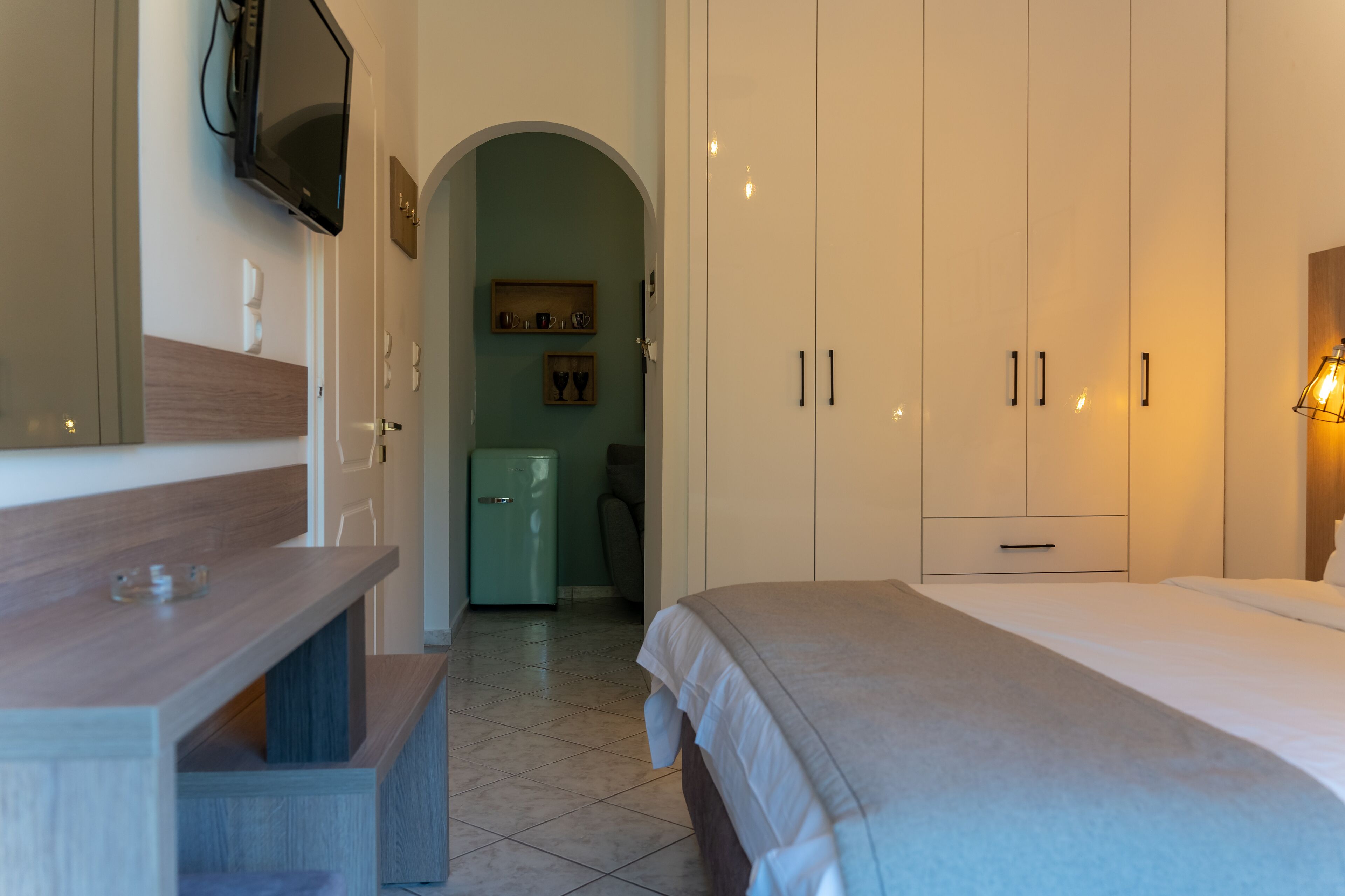 A hotel room with a bed, a desk, a TV mounted on the wall, and a wardrobe.