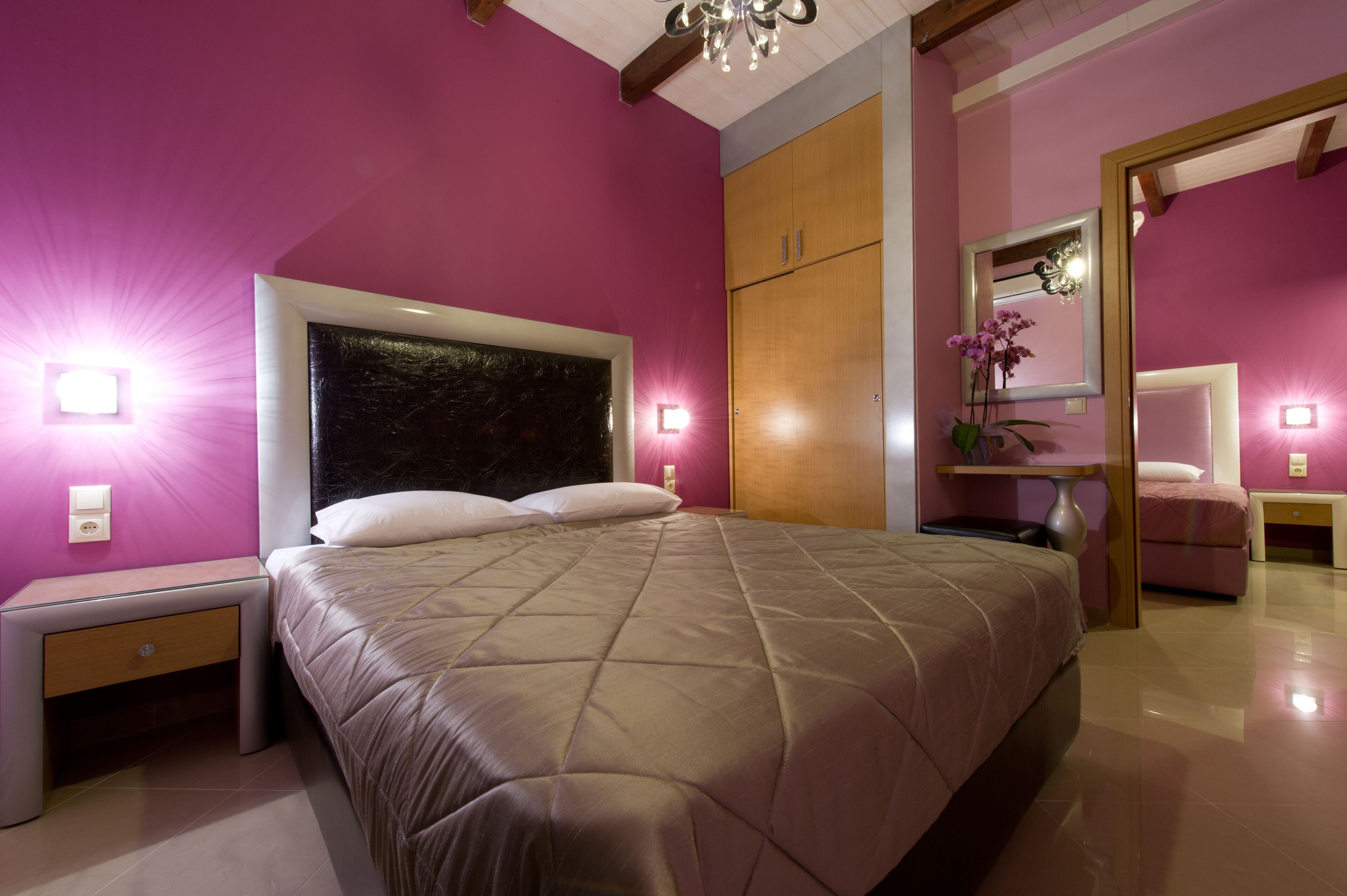 A bedroom with a large bed, wooden wardrobe, bedside table, and a mirror.