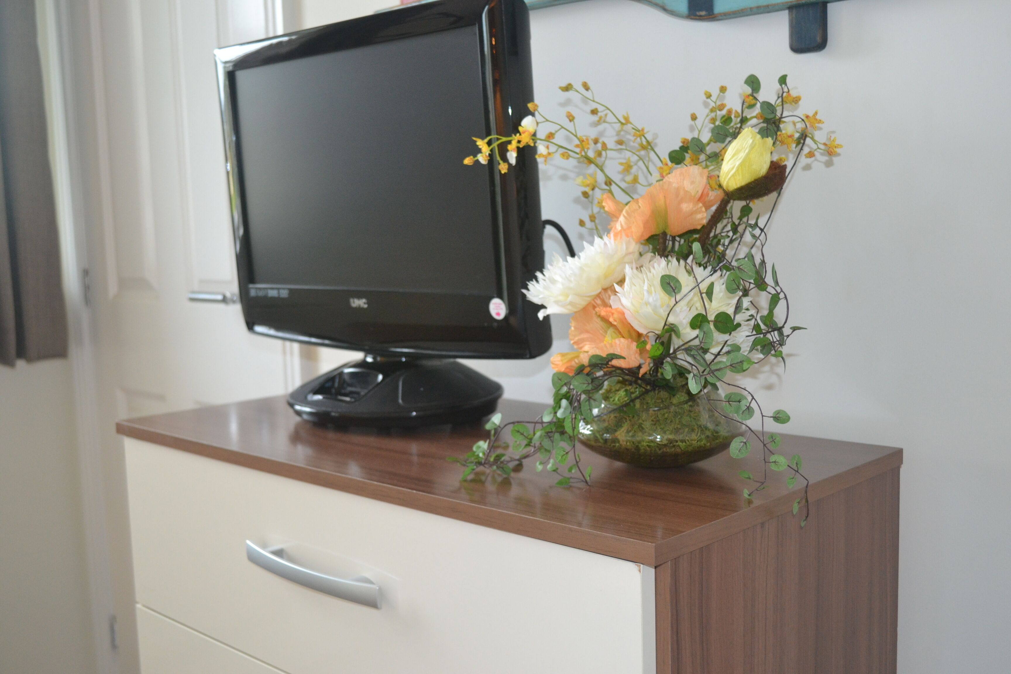 A computer monitor on a wooden desk with a vase of flowers.