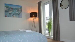 Une chambre à coucher avec un lit, un tableau, une lampe, une fenêtre avec des rideaux et une plante en pot.