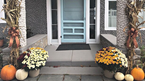 A front porch with a blue door, stone walls, and decorative corn stalks with bows.