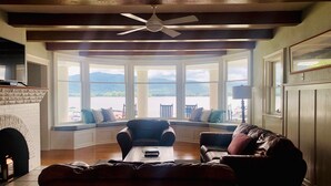 A cozy living room with a fireplace, seating area, and large windows offering a view of the outdoors.