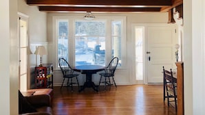 A dining area with a wooden table and chairs, large windows, and a white door.