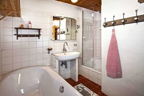 A bathroom with a bathtub, sink, and shower. There is a mirror above the sink and a towel rack on the wall.
