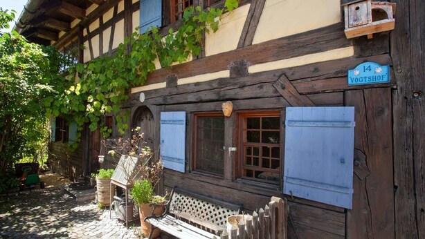 Un edificio tradicional con entramado de madera, un banco de madera y plantas en macetas al frente.
