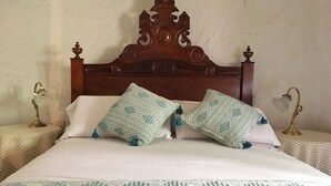 Uma cama com cabeceira de madeira, dois travesseiros estampados e duas mesas de cabeceira com abajures.