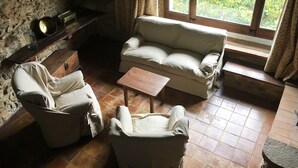 Um quarto acolhedor com parede de pedra, um sofá bege, duas poltronas, uma mesa de centro de madeira e uma janela com cortinas.