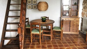 Uma área de refeições rústica com uma mesa de madeira, quatro cadeiras, um candeeiro tecido pendurado e um armário com portas de vidro.
