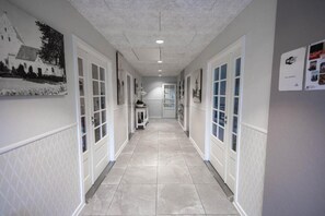 A hallway with white doors, a tiled floor, and wall-mounted pictures. - Hotel Skovpavillonen (Kerteminde)