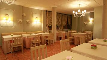 A restaurant with booths, tables, and chairs, featuring a chandelier and wall sconces.