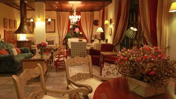 A cozy hotel lobby with wooden furniture, a fireplace, and a dining area.