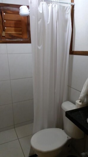 Une salle de bain avec des toilettes blanches, un rideau de douche et un meuble en bois au-dessus des toilettes.