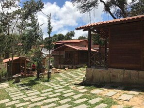 Un edificio rústico de madera con tejado de baldosas, rodeado por un patio empedrado y árboles.