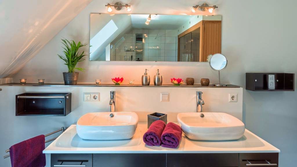 A modern bathroom with two sinks, a large mirror, and a potted plant.